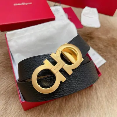 A black leather belt with a large gold double-hook buckle coiled in a red box