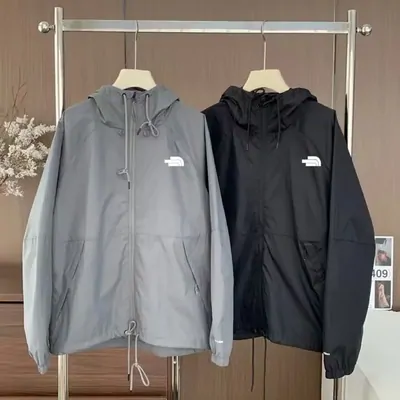 Two hooded shell jackets, one grey and one black, hanging on a steel rack
