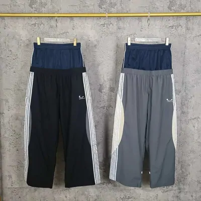 Two pairs of track pants, one navy and one grey, hanging side by side against a grey wall