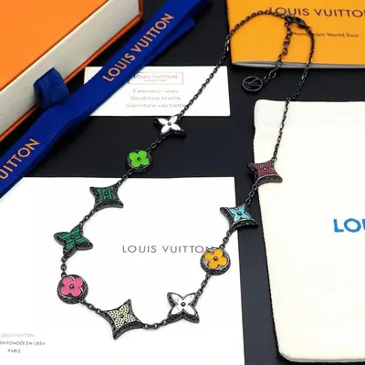 A necklace of multicoloured flower-shaped links laid on a branded orange box, a card and a dust bag